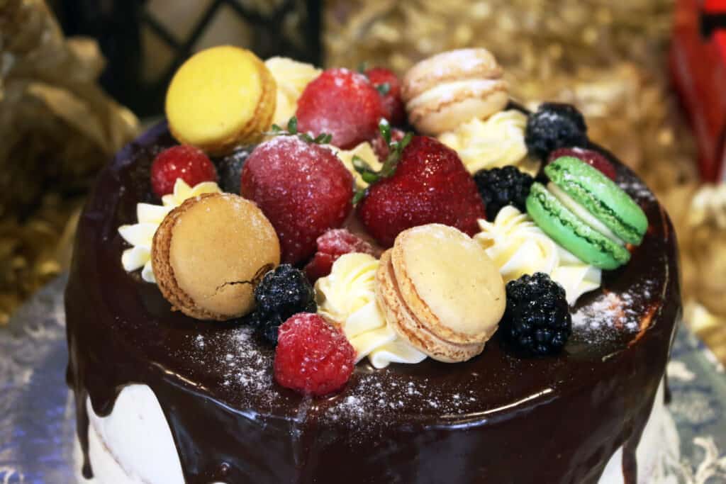 A cake topped with chocolate glaze, macarons, strawberries, raspberries, blackberries, and cream swirls.