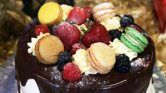 A cake topped with chocolate glaze, macarons, strawberries, raspberries, blackberries, and cream swirls.